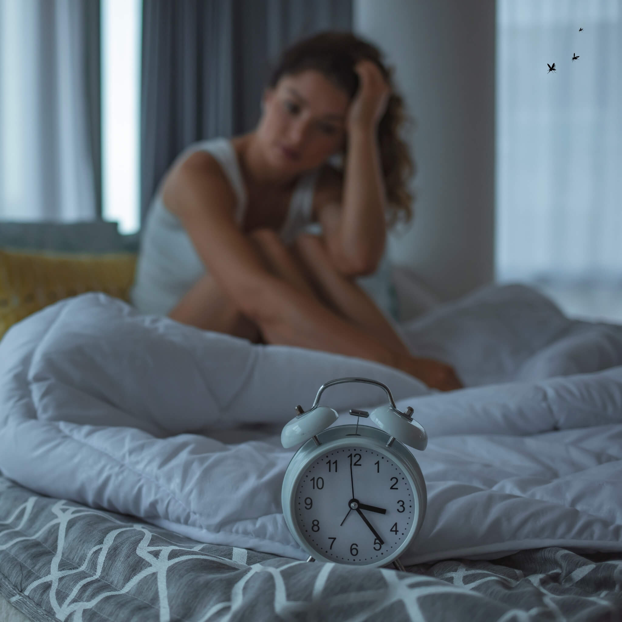 Person sitzt im Schlafzimmer neben einem Wecker